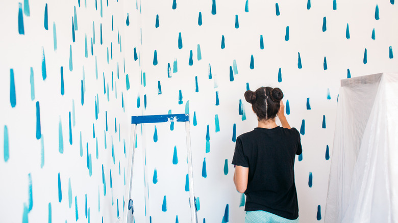 A woman painting a blue geometric pattern on the wall