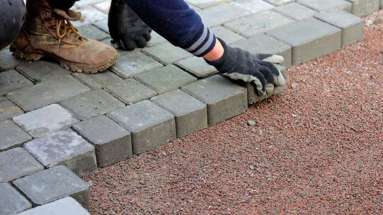 Someone laying down stone pavers over gravel