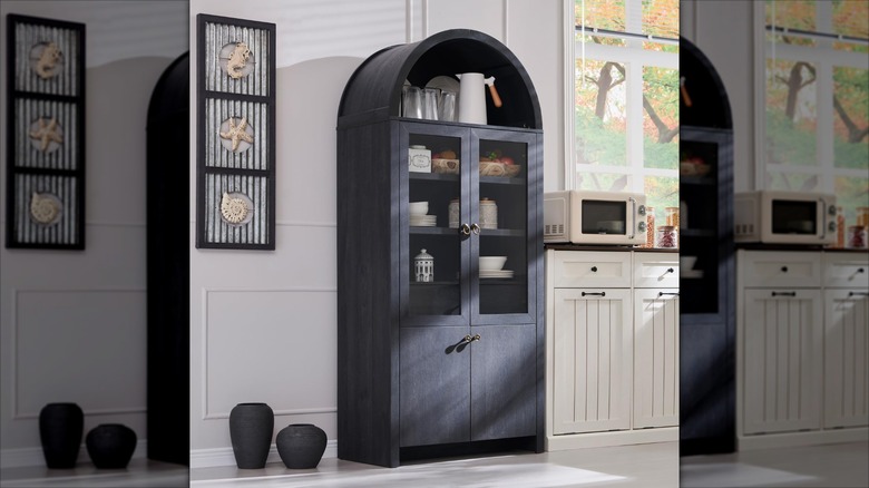 A black curio cabinet with glass doors holds servingware in a white kitchen