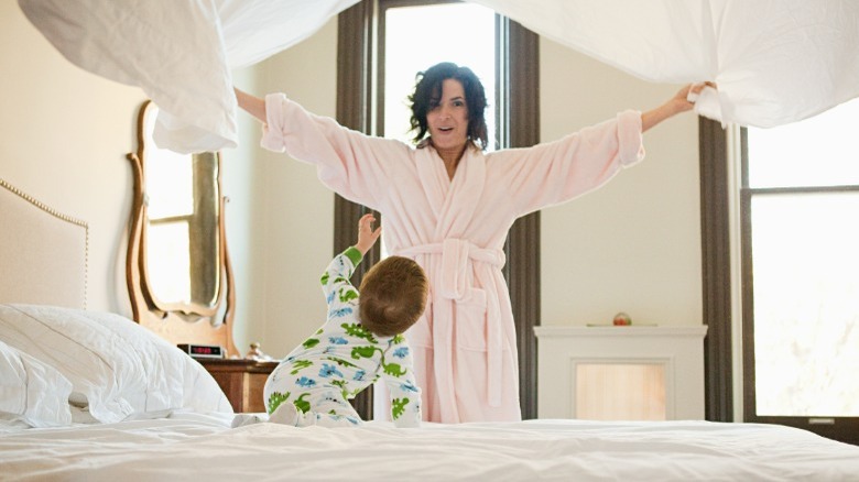 Woman holding up comforter on top of bed with child 