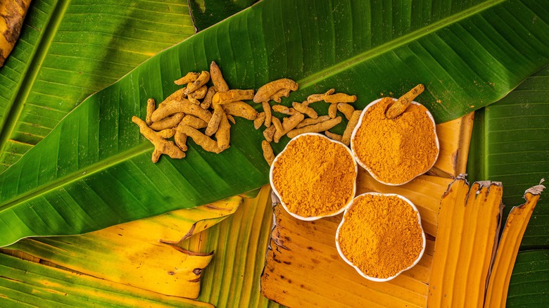 Turmeric rhizomes and ground turmeric bowls on top of leaves