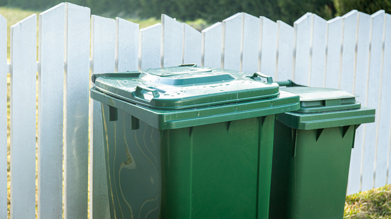 Trash bins behind white fence