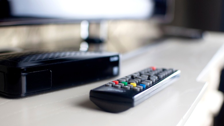 Remote and cable box sitting on white console in front of TV