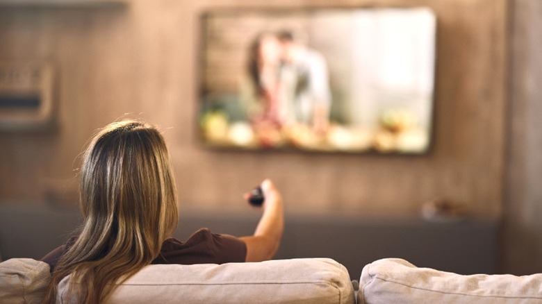 Woman watching TV while sitting on couch and holding a remote