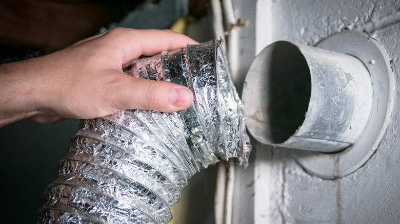 Person connecting a dryer vent hose to a vent outlet