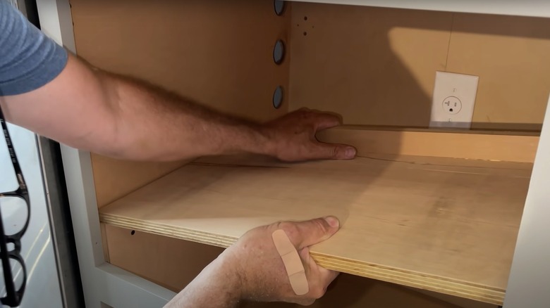 person installing a shelf in a kitchen cabinet