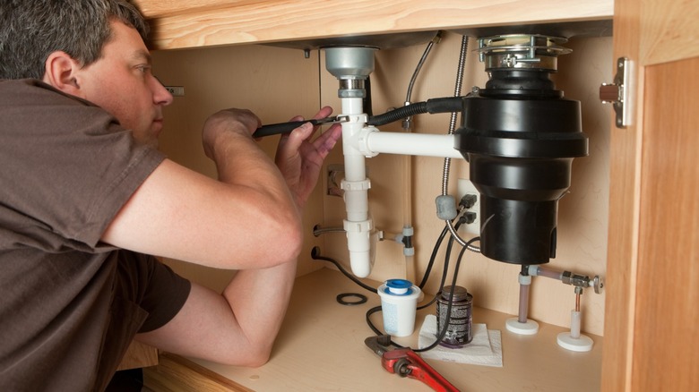 A man uses a hand tool to attach plumbing to a garbage disposal