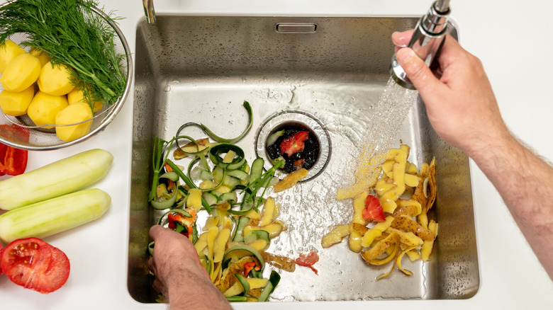 A person rinses food scraps down a kitchen sink drain