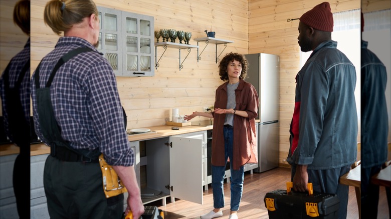 A young woman talks to two tradesmen in her kitchen