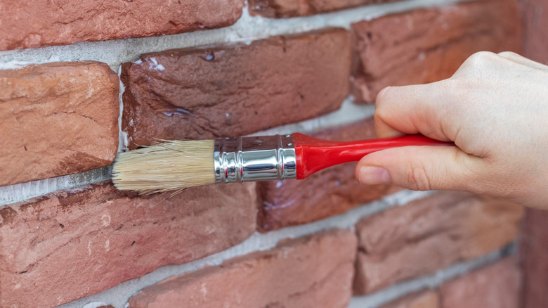 Person varnishing grout on a brick feature wall