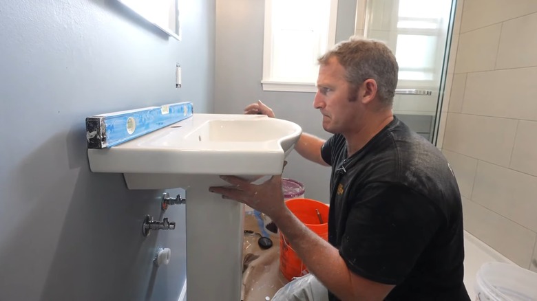 repair man leveling pedestal sink during installation