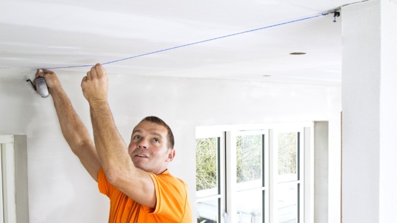 Man snapping chalk line on drywalled ceiling