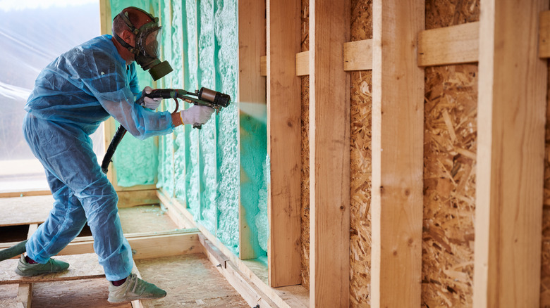 A professional applies green spray foam in between garage studs