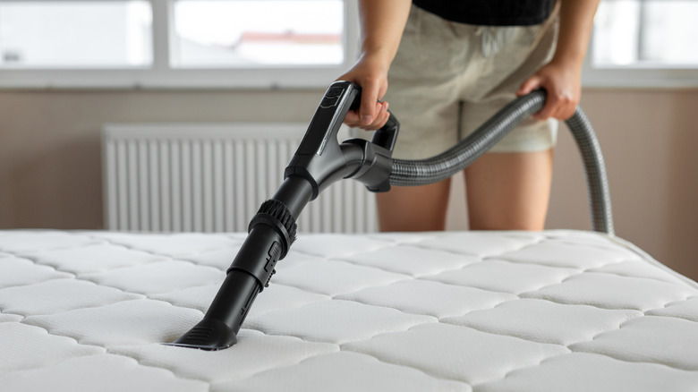 Person vacuums bare mattress with attachment