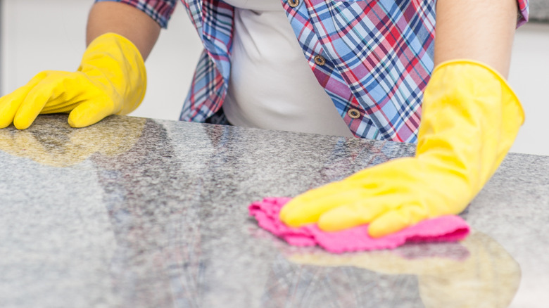 person wiping countertop with rubber gloves