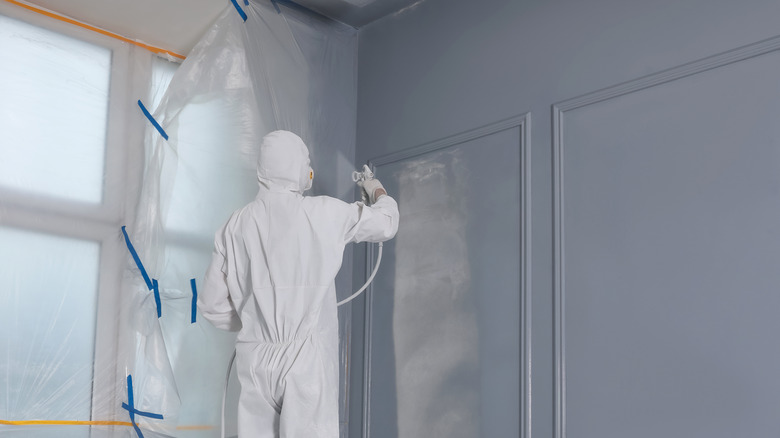 Person in coveralls spraying wall paint