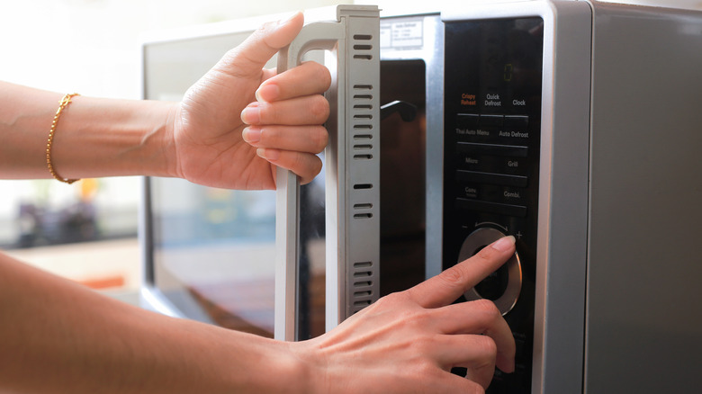 person pushing buttons on microwave