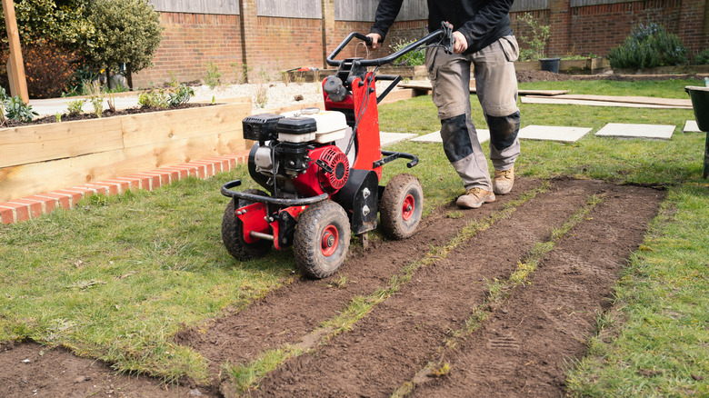 A man using a mechanical turf cutter to clear the soil for artificial grass