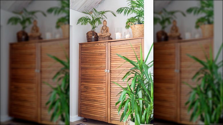 slatted armoire with potted plants, candles, and a buddha statue on top