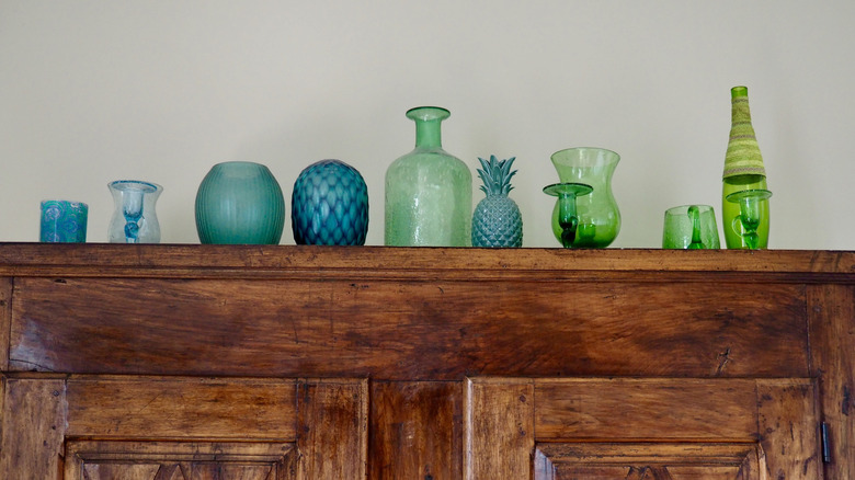 Collection of blue and green vases and candle holders on top of wooden armoire