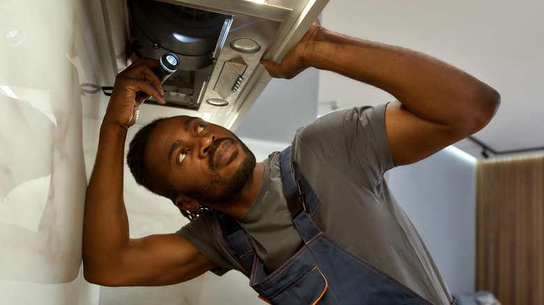 technician peering into range hood 