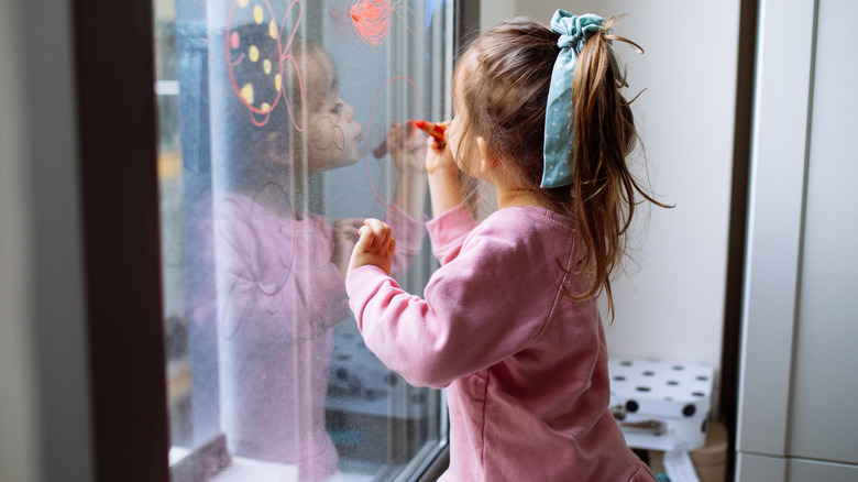 little girl drawing on window