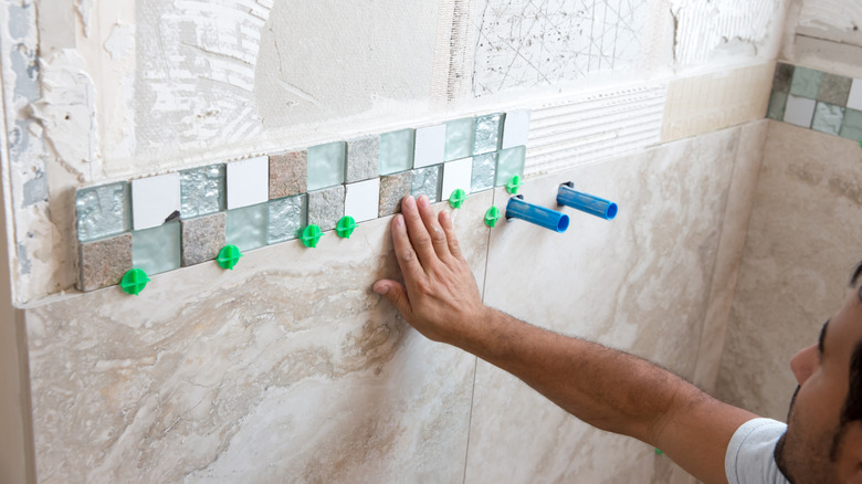 A man installing small mosaic tiles in multiple materials