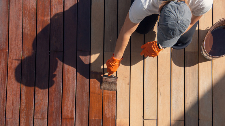 Worker applying wood deck sealer with brush to individual panels