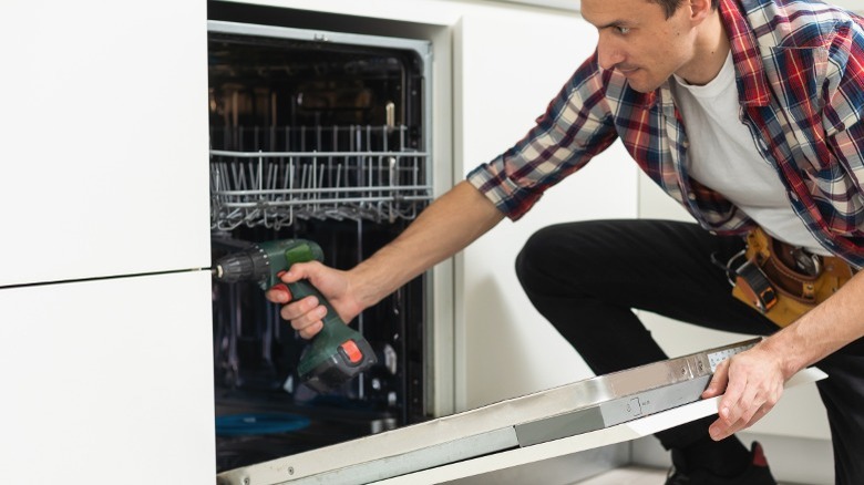 man screwing dishwasher into cabinets