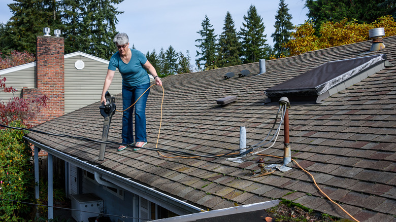 Woman clearing gutter with leaf blower