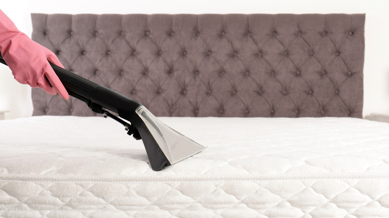 Gloved hand vacuuming mattress