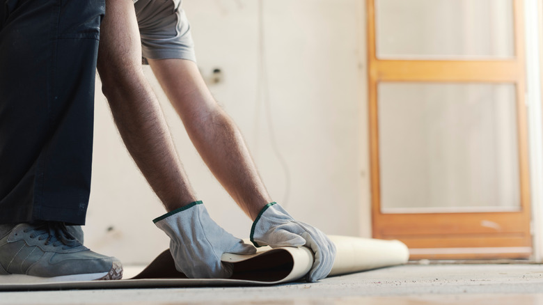 A man wearing gloves and removing linoleum flooring