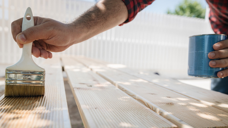 A person applies a stain remove to wooden boards with a paintbrush