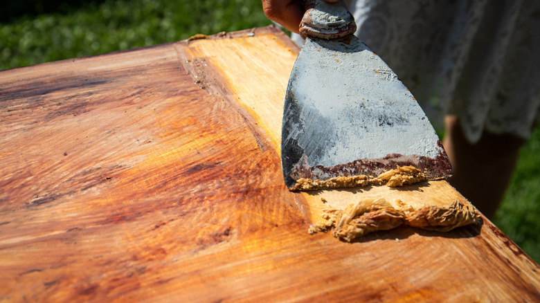 Person scrapes stain off a wooden table with a putty knife