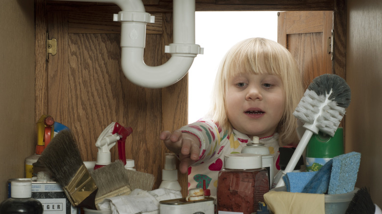 kid and items in under-sink cabinet