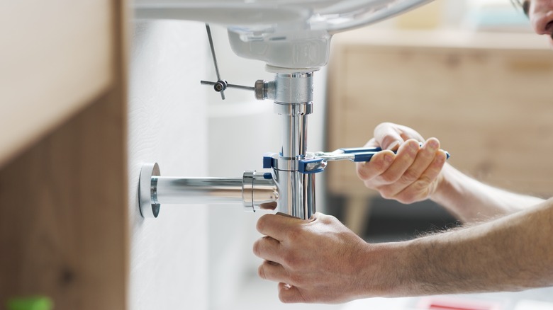 Person working on plumbing under bathroom sink