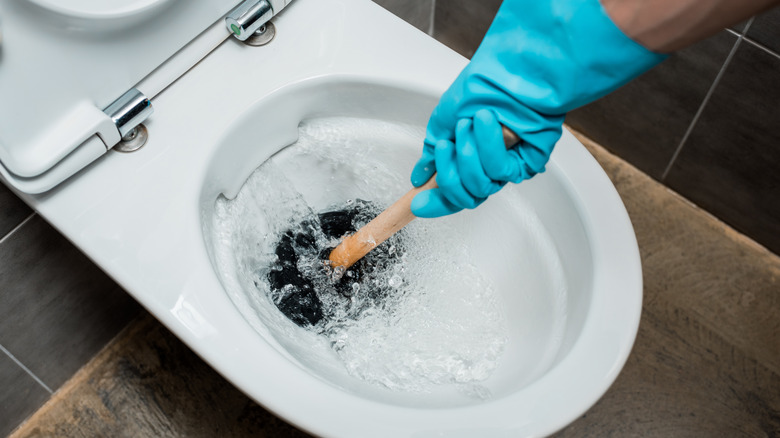 person using plunger on toilet