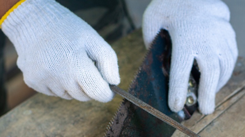 person wearing gloves while sharpening a saw