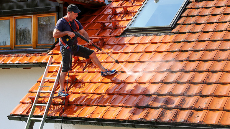 A man cleans a clay tile roof using a pressure washer