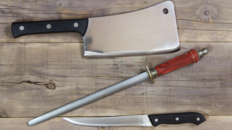 A cleaver with a honing rod rests on a wood surface