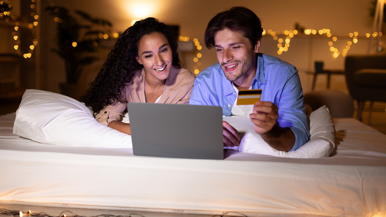 A man and a woman lying on a mattress while online shopping