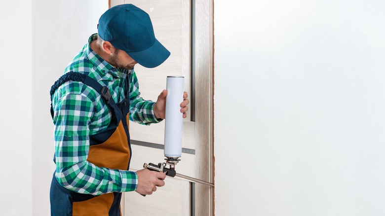 A handyman seals a door frame.