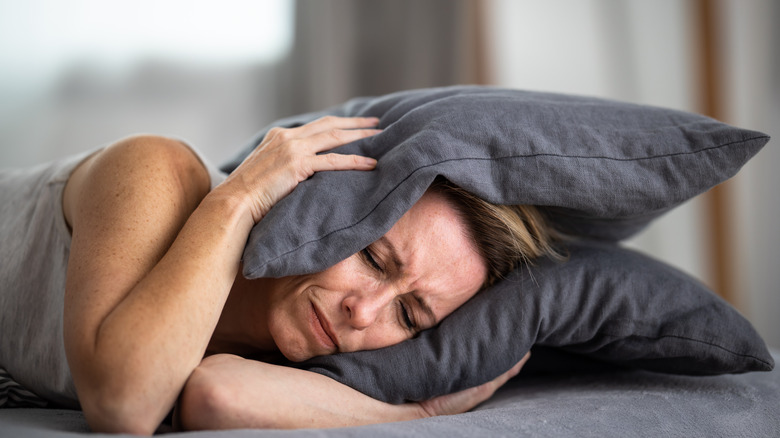 A woman having trouble sleeping, attempting to cover her ears with a pillow.