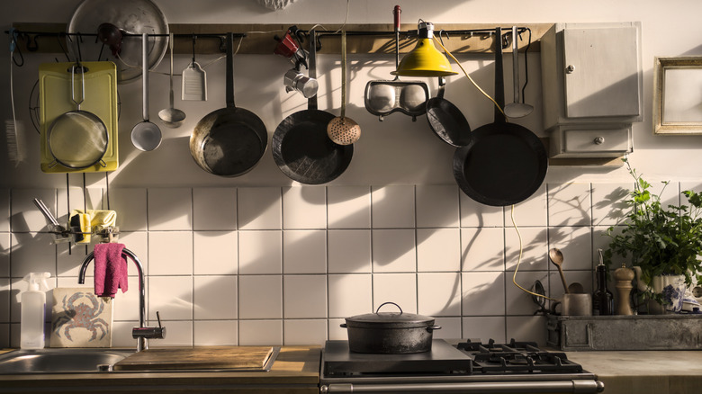 Several cookware items hanging up in a kitchen above a stove and sink