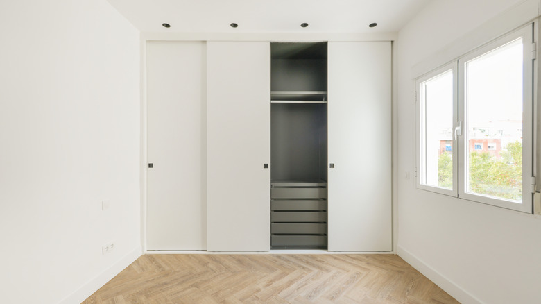 An empty bedroom with a boring closet with white sliding doors