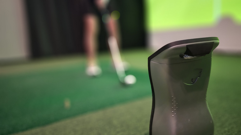 A golf launch monitor with a golfer in the background