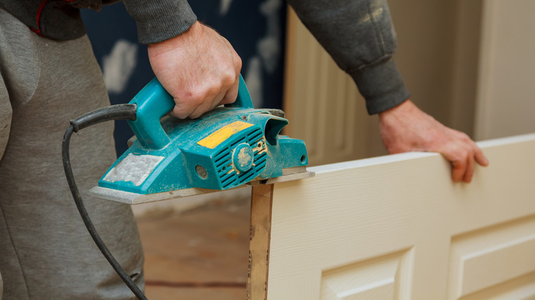 A person uses a sander to trim a door