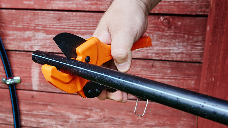 Person using pipe cutter to trim black pipe