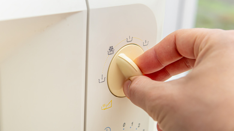 Hand moving the knob of a white oven to defrost