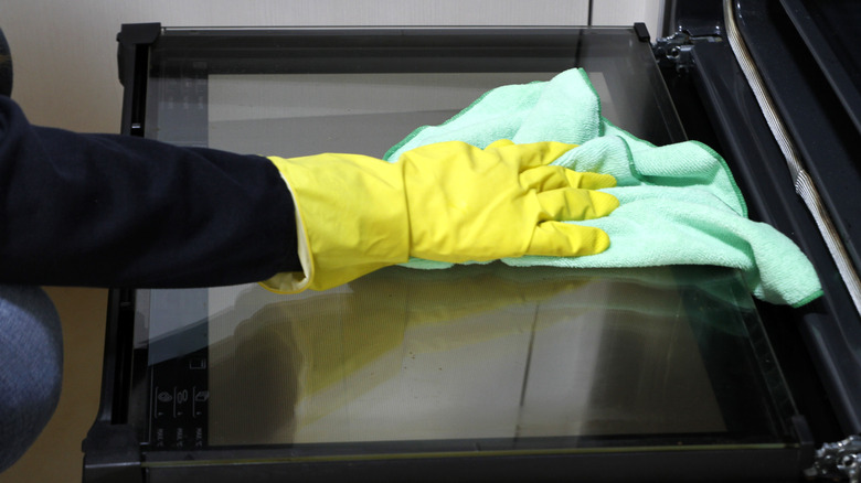 Hand wearing yellow gloves and wiping oven door